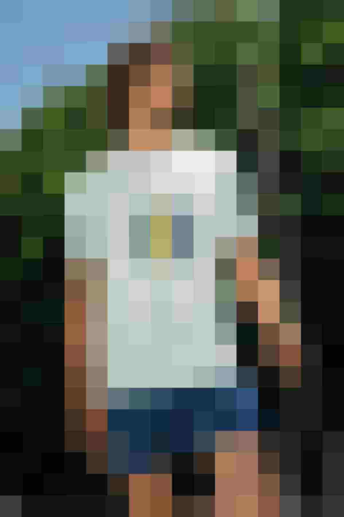 Mann in hellblauem T-Shirt und kurzen Hosen im Freien, umgeben von Bäumen.