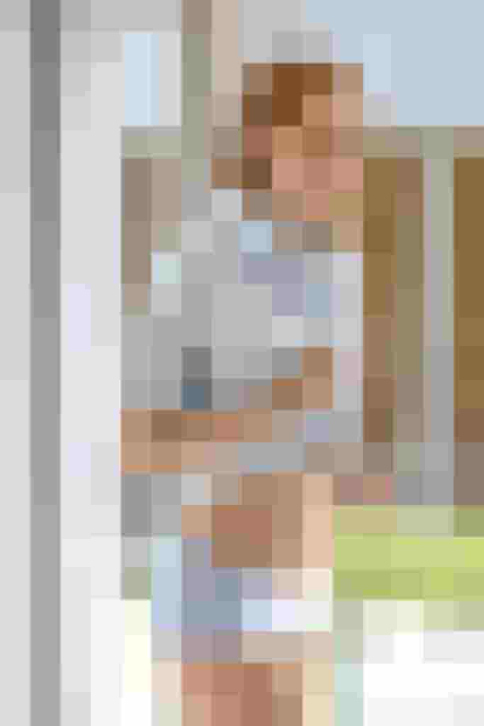 Lächelnde Frau in gestreifter Bluse und blauer Unterwäsche vor Fenster, betont modernen Stil.