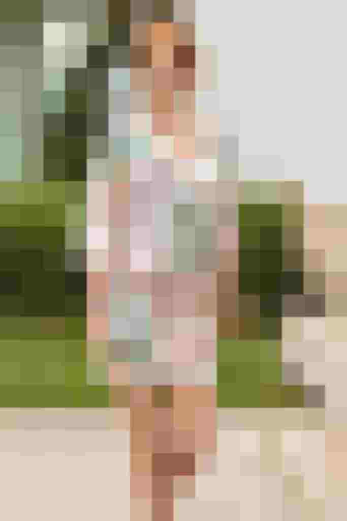 Model in blumigem Kleid, lässig gehend vor grünem Hintergrund. Elegante Bademode für Damen.