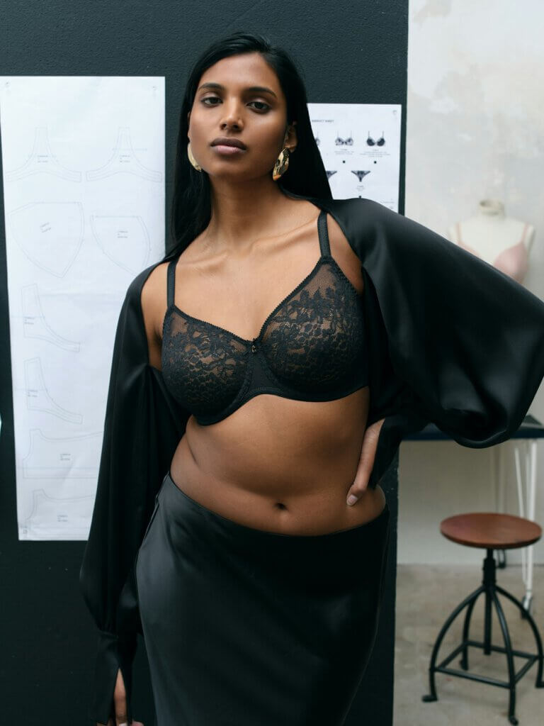 Dame mit schwarzer Spitze und Satinrock vor skizzenhaftem Wäschedesign, stilvoll und elegant.