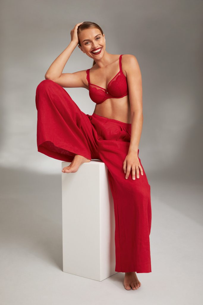 Frau in rotem Spitzen-BH und roter Hose sitzt lächelnd
