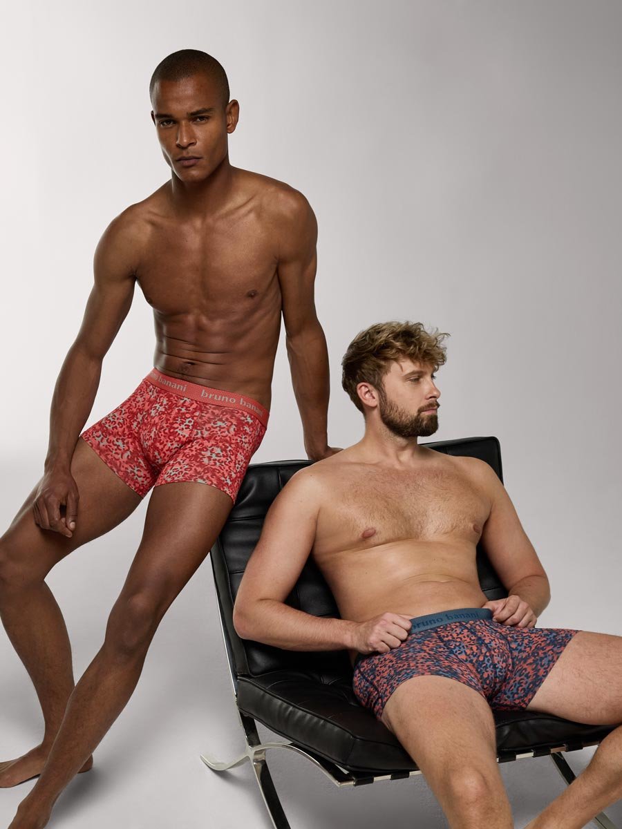 Zwei Männer präsentieren gemusterte Boxershorts in einem Studio, einer stehend, einer auf einem schwarzen Stuhl sitzend